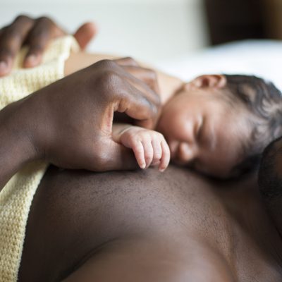 A father lying down with his newborn baby daughter sleeping on his chest.